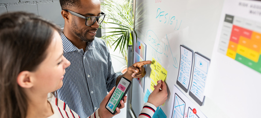 [Featured Image] Two people map out a mobile app design on a whiteboard.