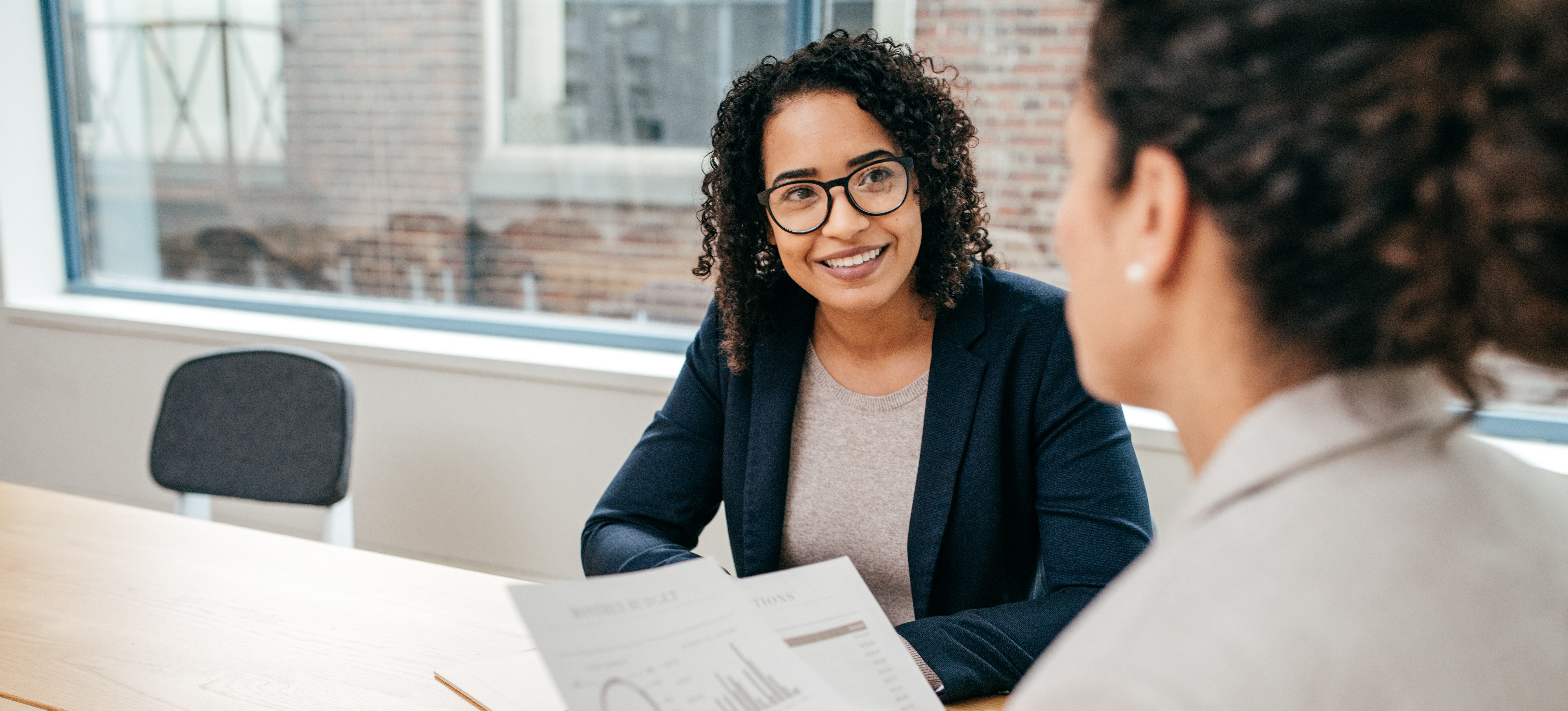 [Featured image] Two executive MBA students sit at a table near a window and review reports.