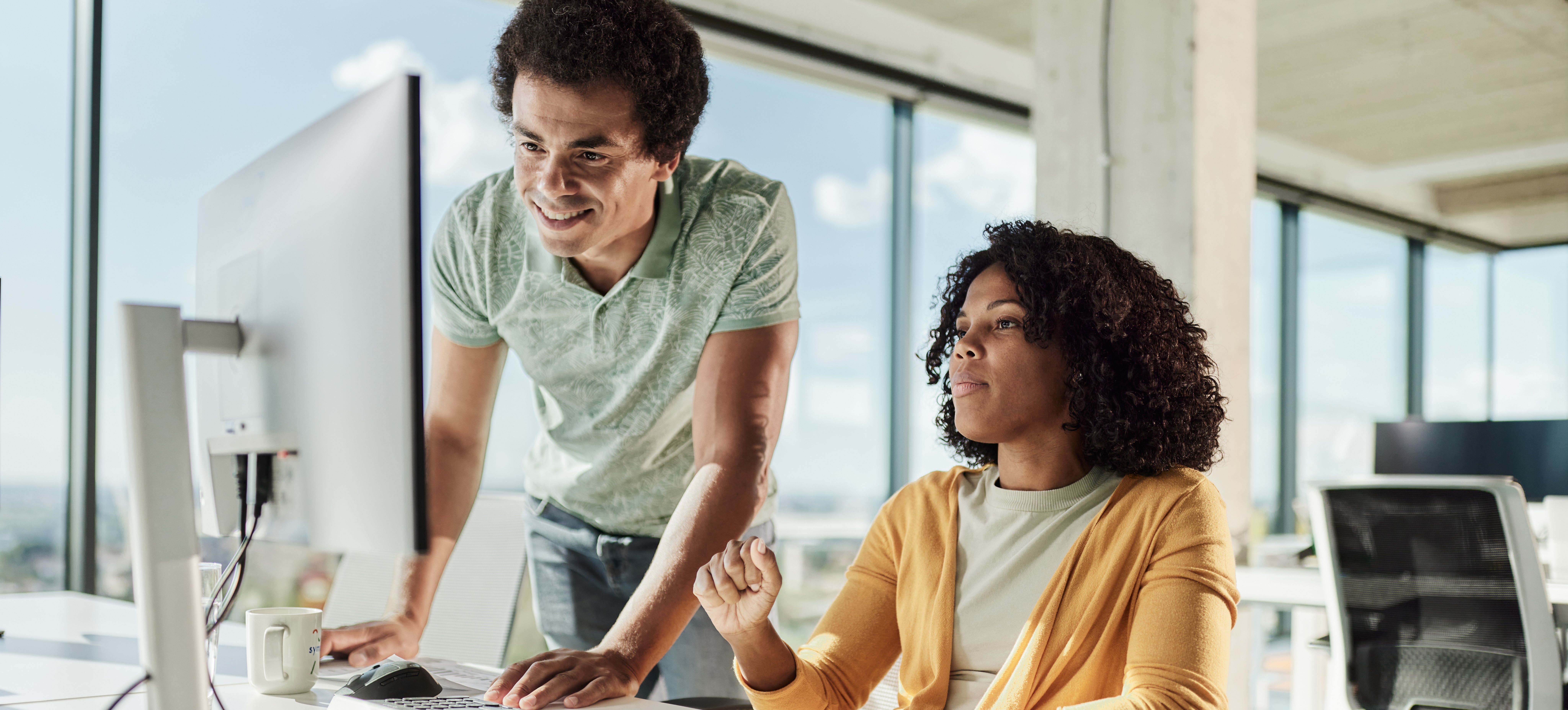 [Featured Image] Young software programmers discuss the merits of GitLab vs. GitHub while looking at a computer screen in a workspace with plenty of windows. 
