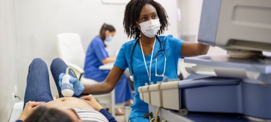 [Featured image] A sonographer wearing blue scrubs performs an ultrasound on a patient. 