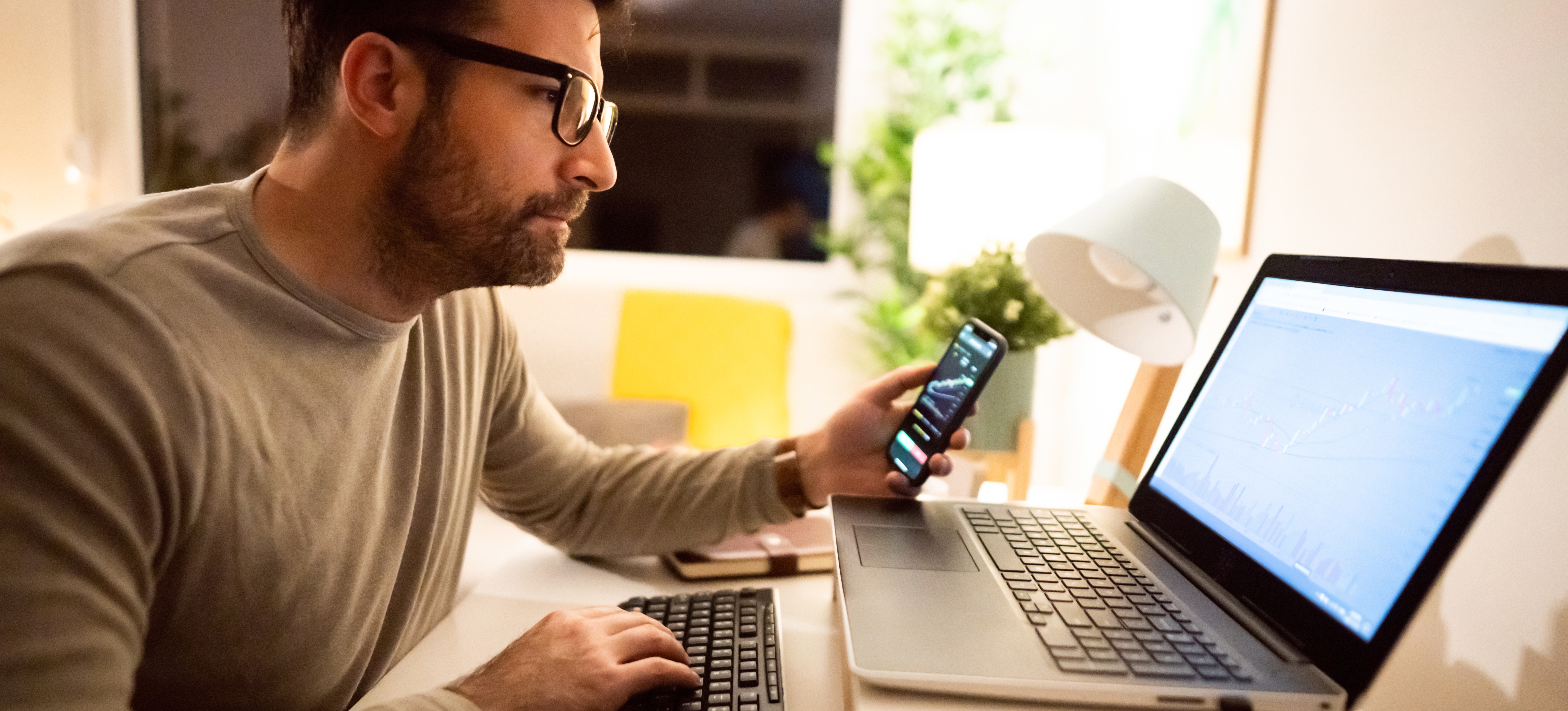 [Featured Image] Male trader follows crypto patterns on computer and phone to know when to invest.