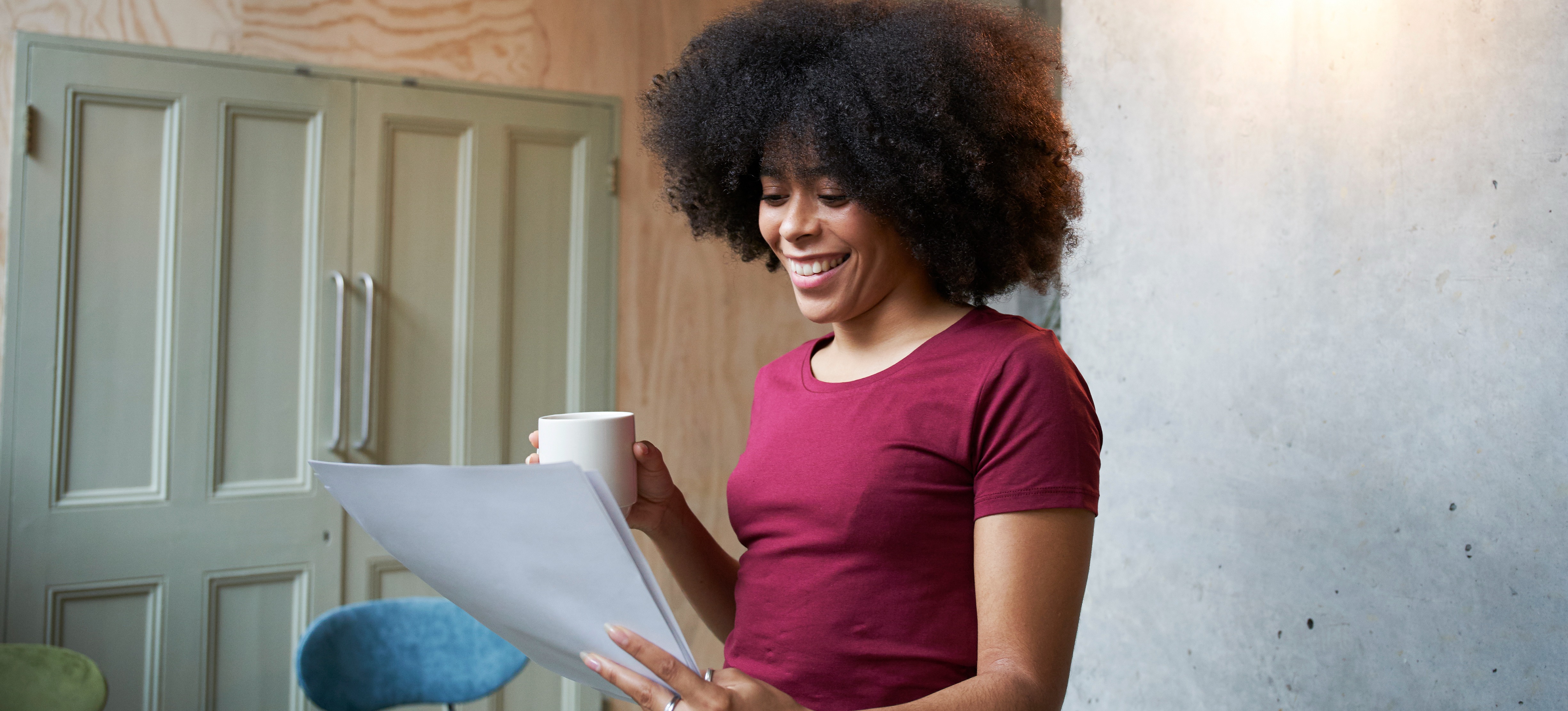 [Featured image] A person in a maroon shirt holding a cup of coffee looks over a cover letter and smiles.