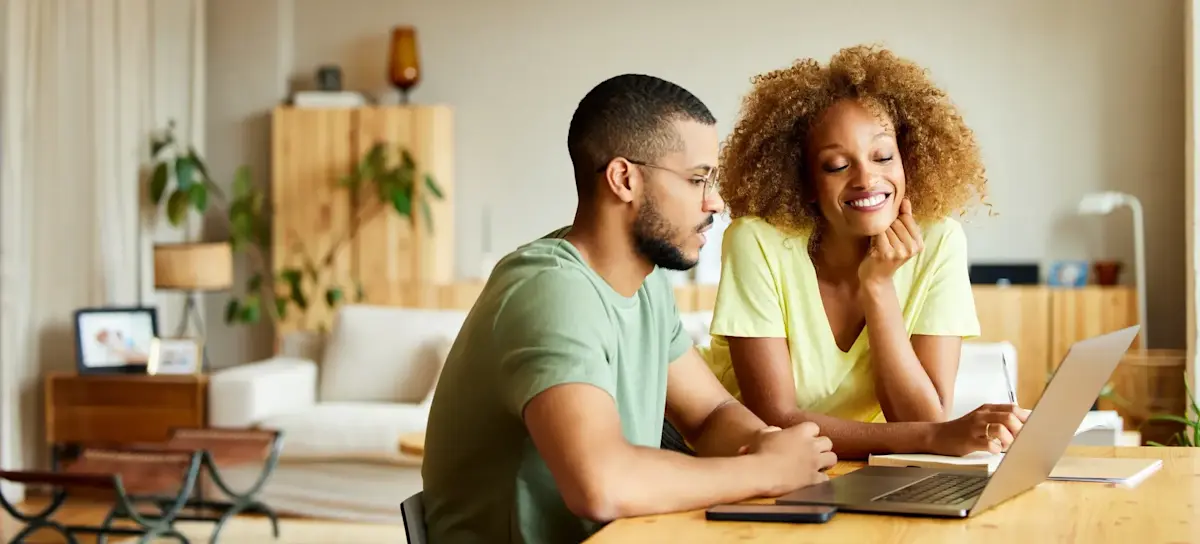 [Featured Image] A happy couple sits at a table in their living room, learning about Excel to XML conversion on their laptop.