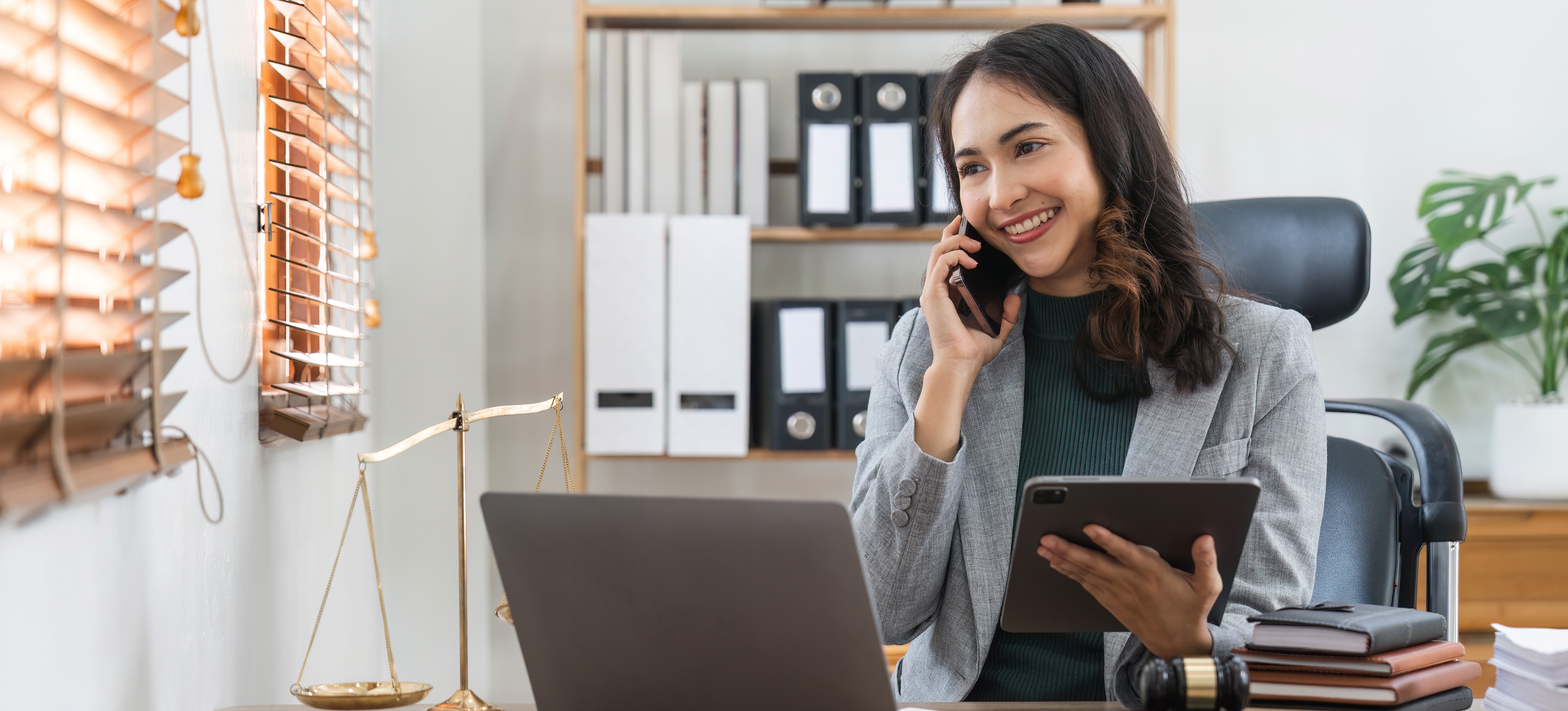 [Featured Image] A trial attorney, one of many DOJ jobs, sits in her office, talks on the phone, and uses a tablet.
