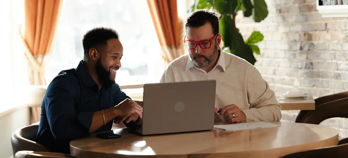 [Featured Image] A young professional meets with their mentor to discuss their plan for advancing on their deep learning career path, while showing them potential certifications and learning opportunities on their laptop in a relaxed environment.