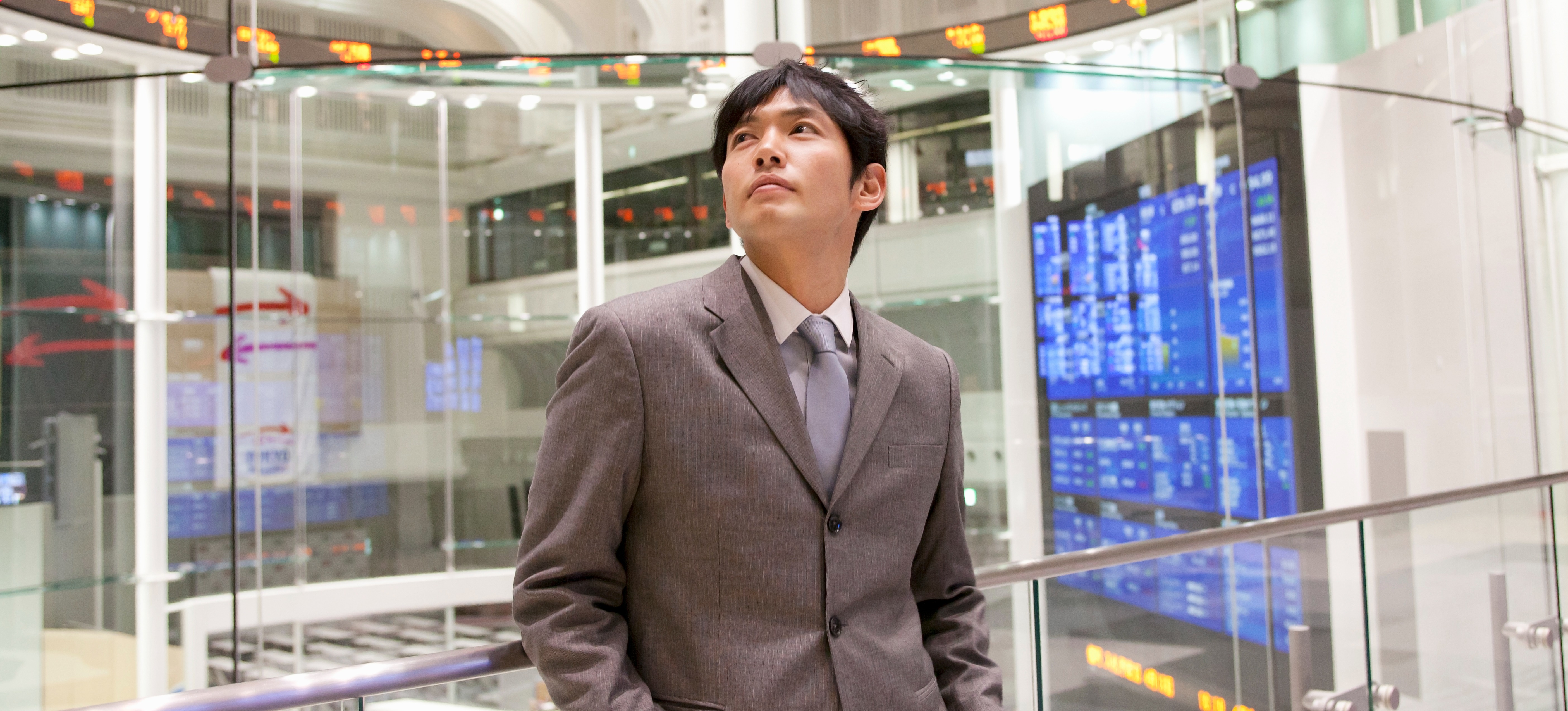 [Featured Image] A businessman stands in the Toyko Stock Exchange and looks at many displays of stocks, which are analyzed using descriptive statistics.
