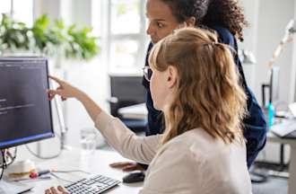 [Featured image] Two colleagues discuss a potential threat at their cybersecurity jobs in NYC. 