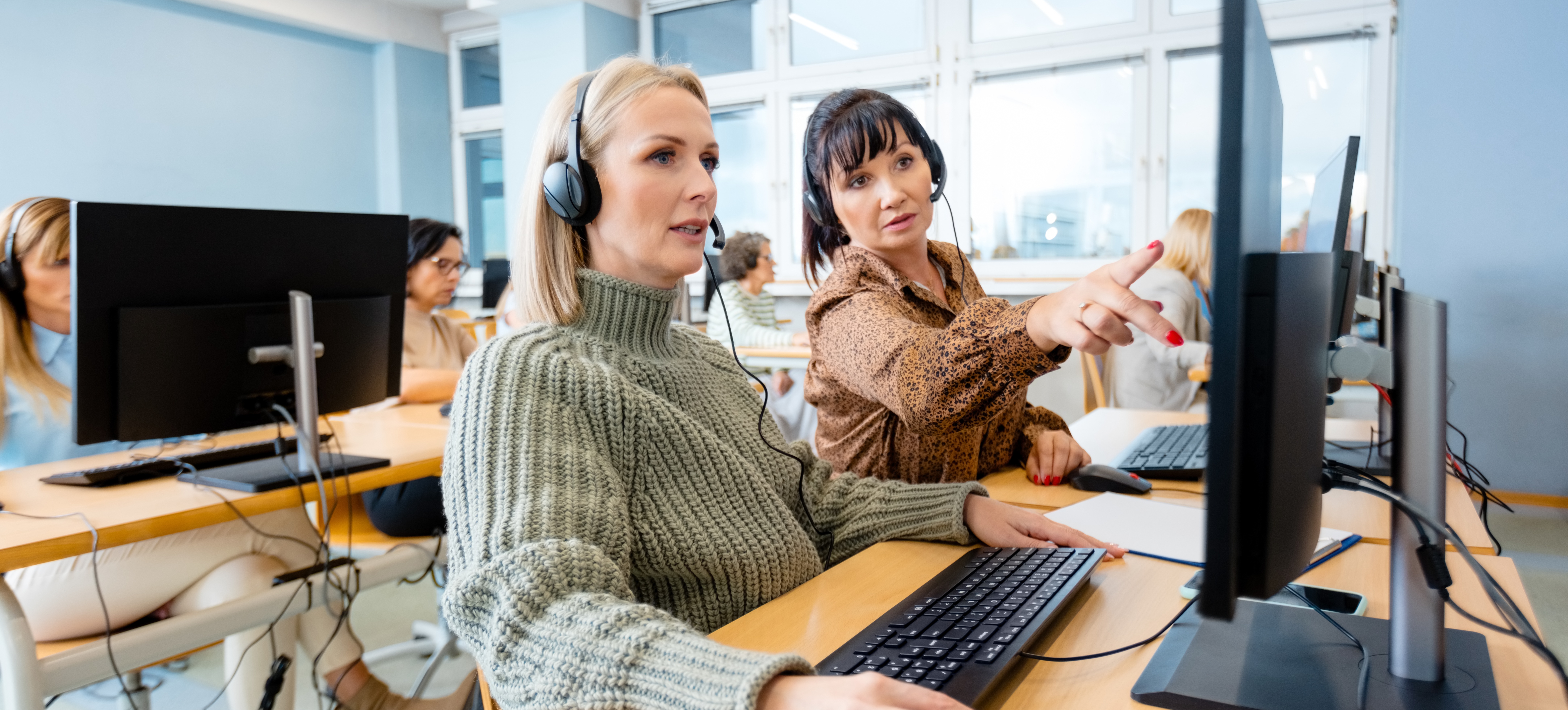 [Hauptbild] Zwei Kollegen mit Kopfhörern sitzen an Computern und nehmen im Rahmen der Weiterbildungsstrategie ihres Unternehmens an Online-Kursen teil.