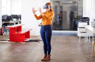 [Featured Image] A woman stands in an office wearing a virtual reality headset.