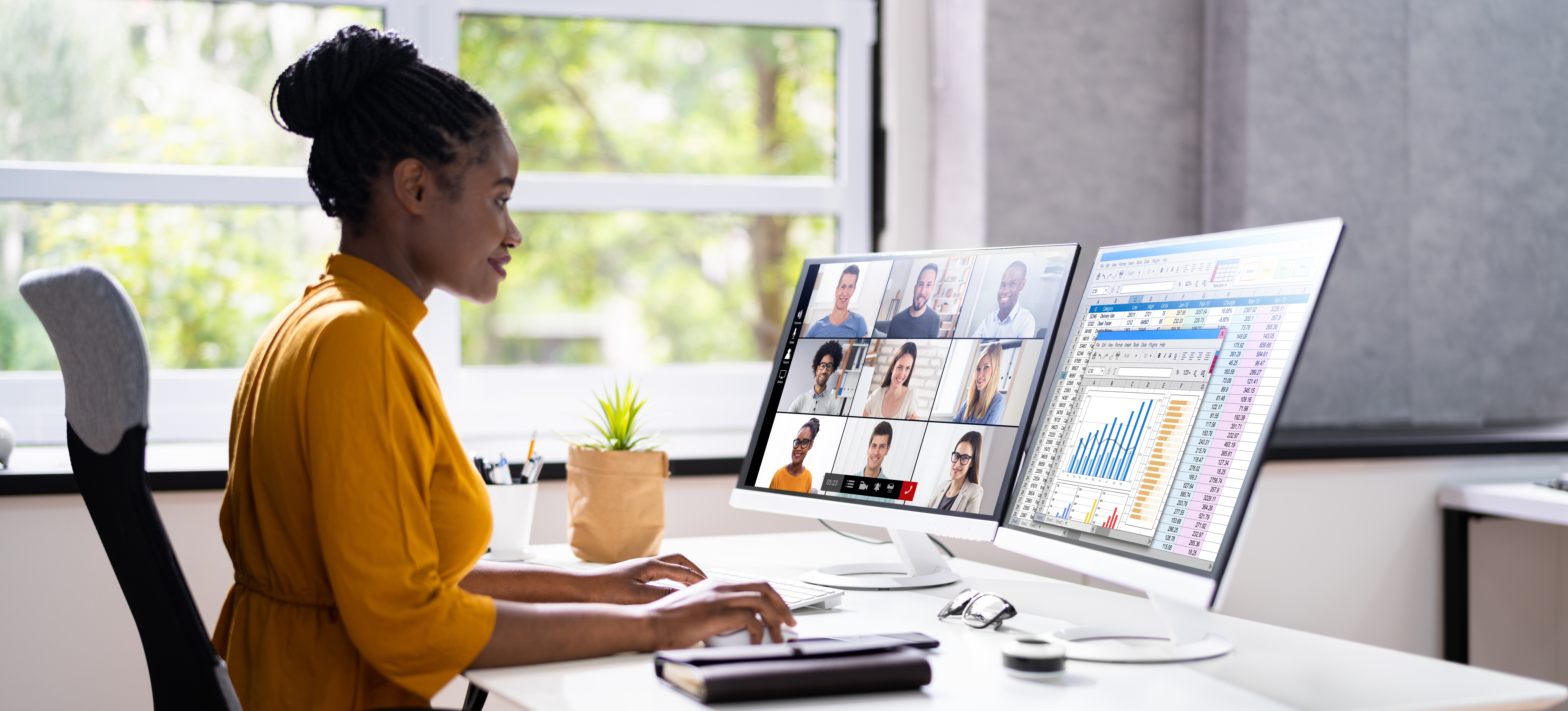 [Featured Image] A professional sits at her desk and uses software as a service to have a video conference with colleagues on one computer screen while consulting data on her second computer screen.