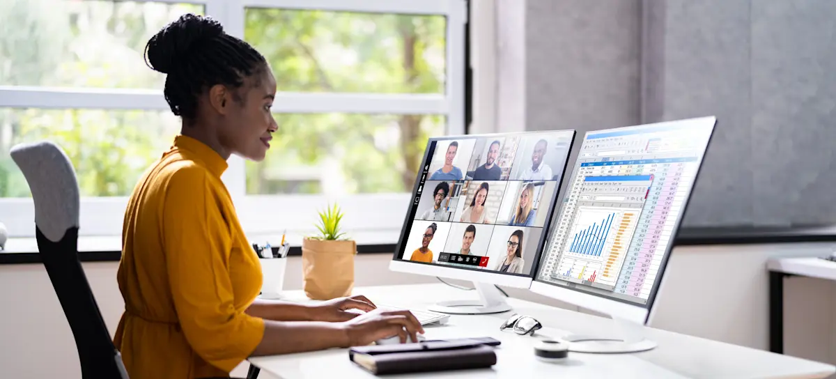 [Featured Image] A professional sits at her desk and uses software as a service to have a video conference with colleagues on one computer screen while consulting data on her second computer screen.