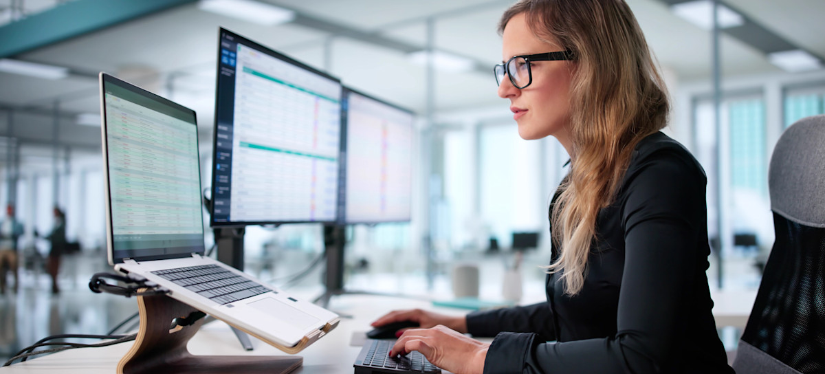 [Featured Image] A financial professional progresses through the accounting cycle while working with data on a computer in an open office.
