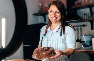 [Featured image] A food influencer holds a cake and smiles in front of a video camera.