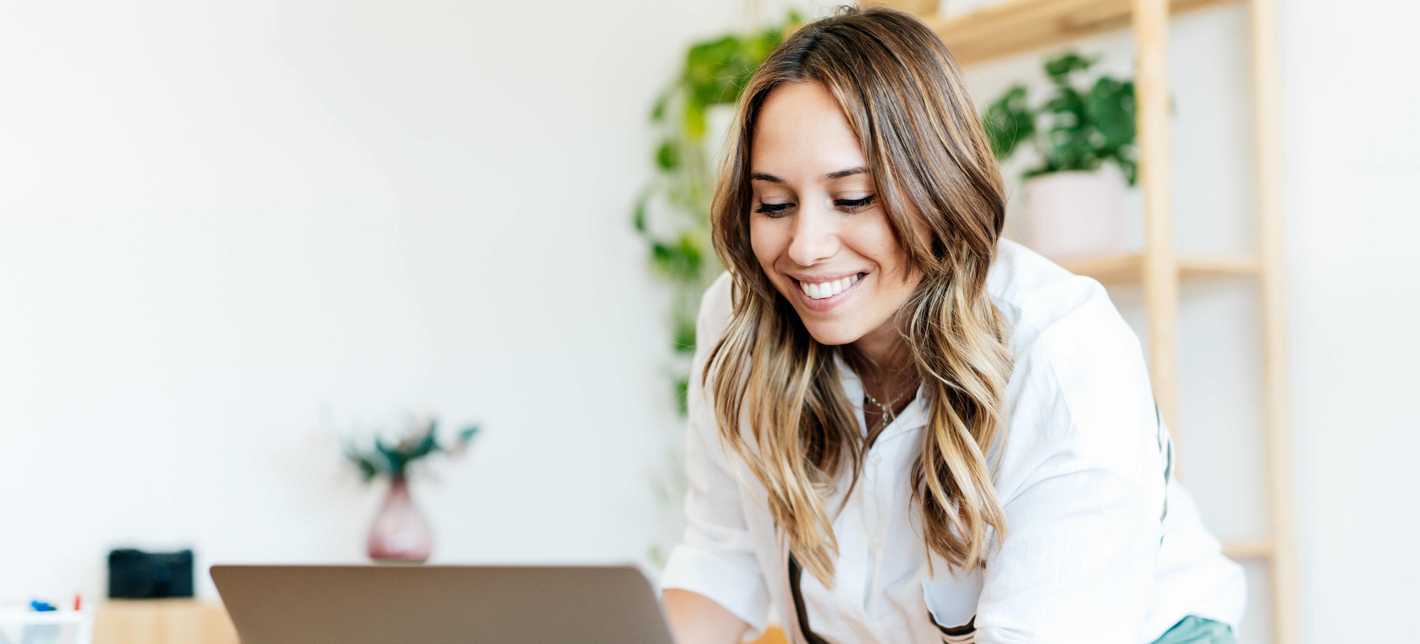 [Featured Image] An HR professional smiles at their laptop after learning about various HR certifications available online to advance their career. 
