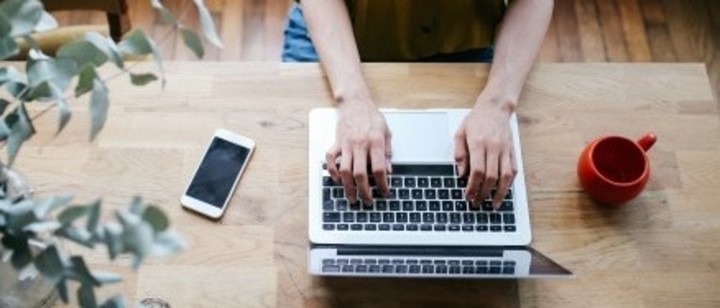 Hands are typing on a laptop keyboard at a desk
