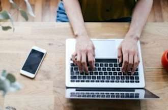 Hands are typing on a laptop keyboard at a desk