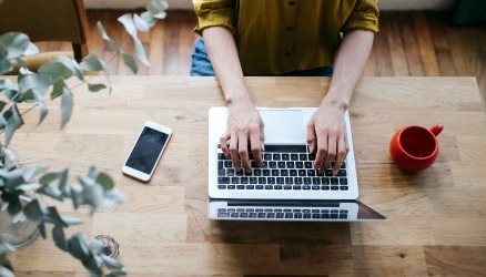 Hands are typing on a laptop keyboard at a desk