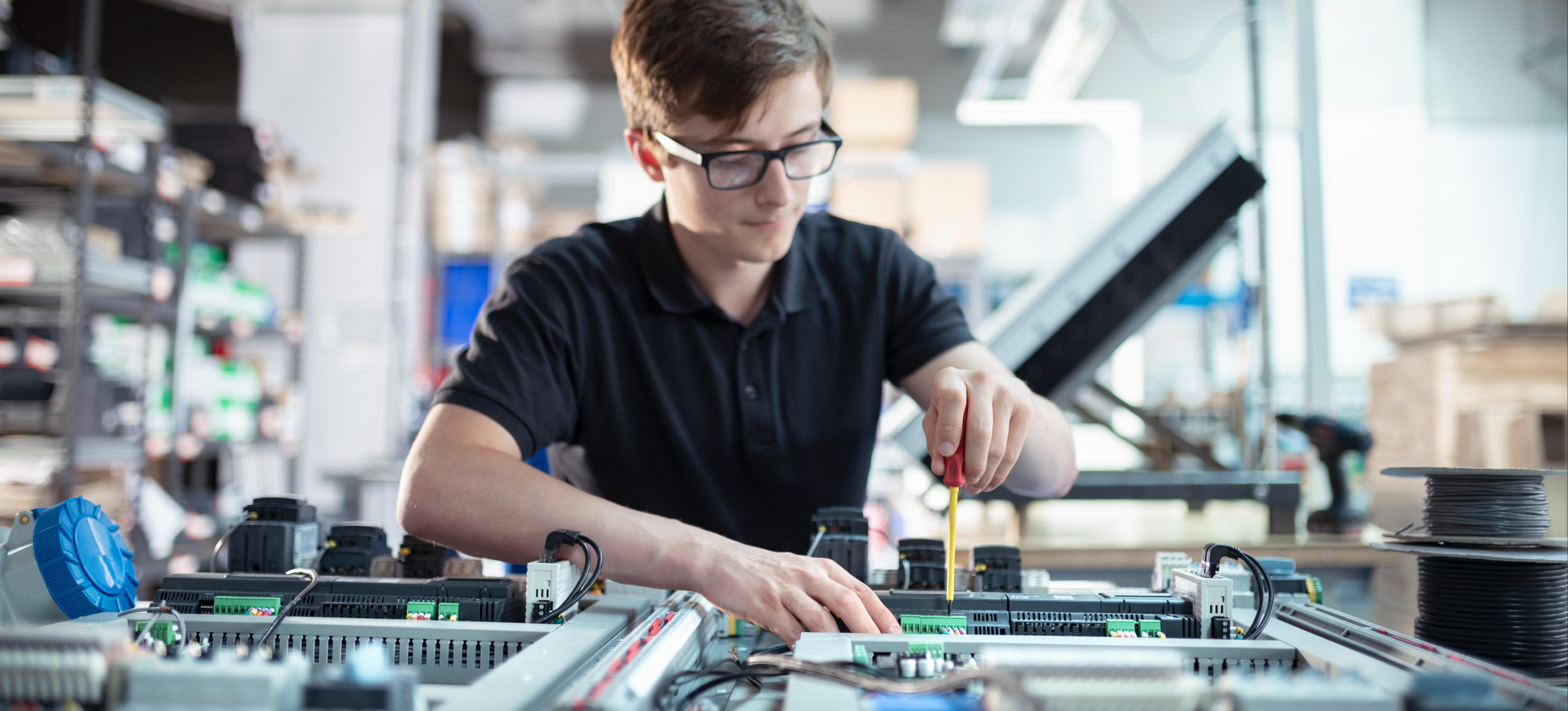 [Featured Image] A controls engineer works on machinery with tools in a manufacturing organization.