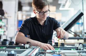 [Featured Image] A controls engineer works on machinery with tools in a manufacturing organization.