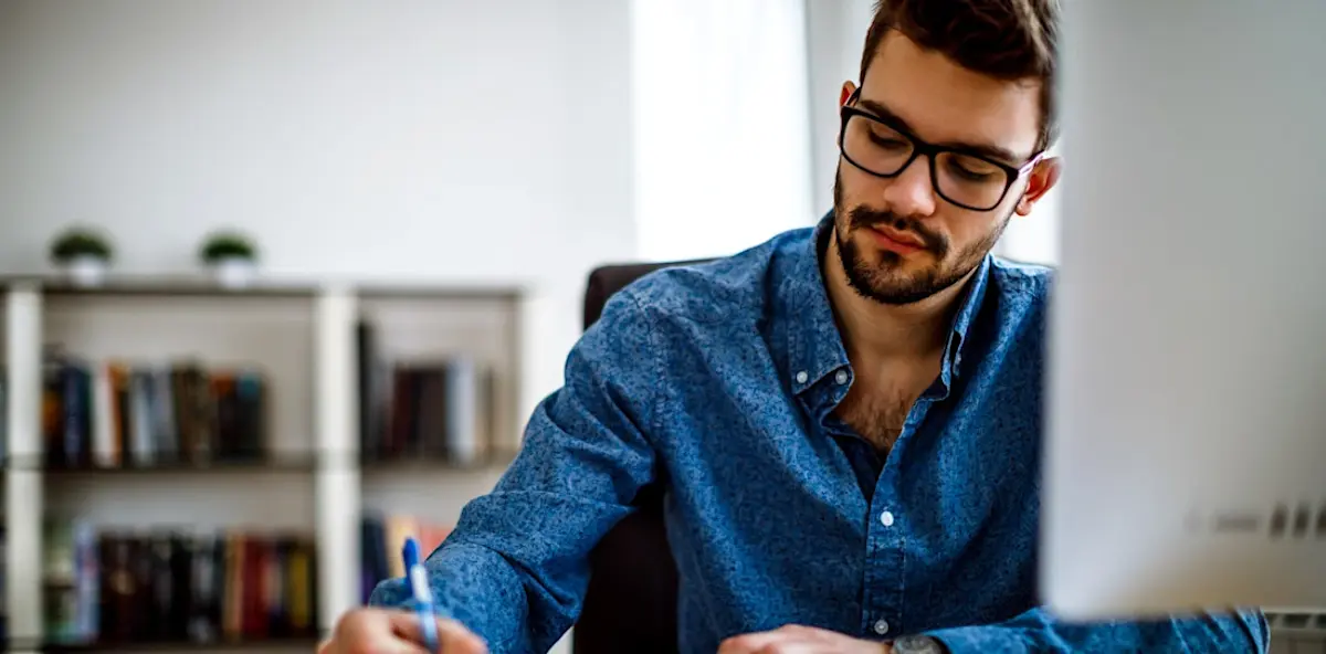 A person with glasses and a blue shirt working on their master's degree in front of a computer