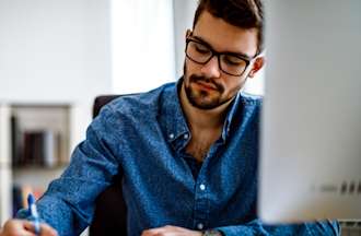 Man with glasses and a blue shirt working on his master's degree in front of a computer