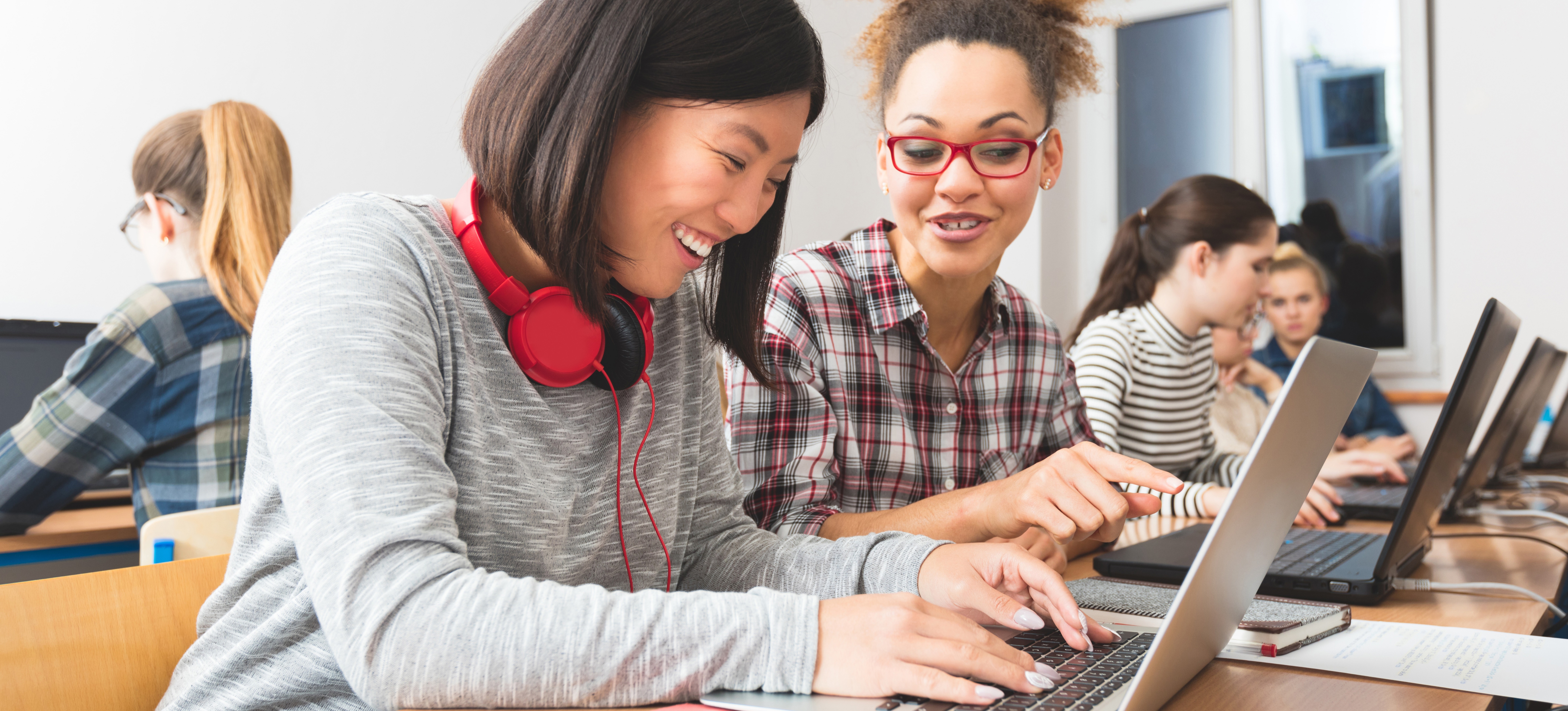 [Featured image] Two learners practice writing Python code on their laptops in a classroom lab setting.