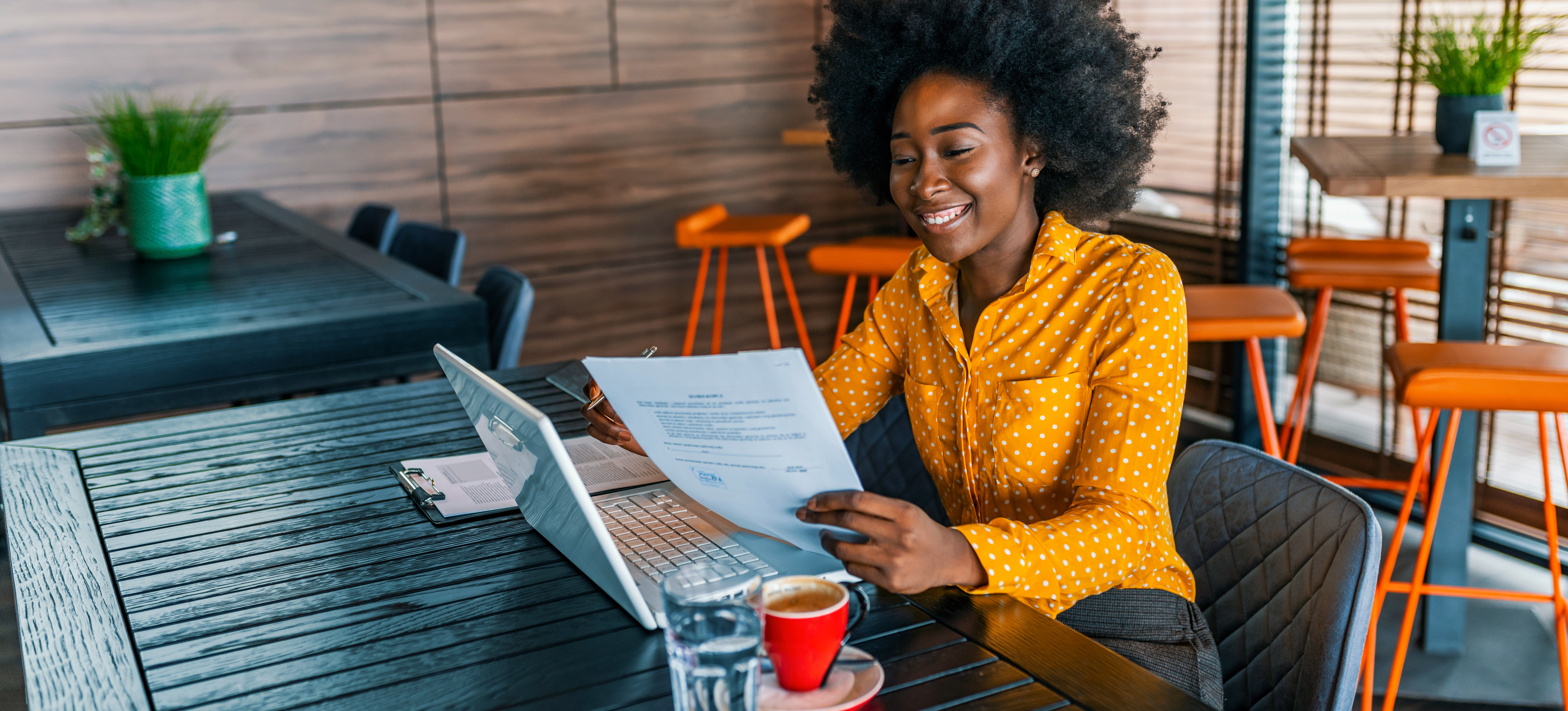 [Featured Image]: A job seeker with curly hair and in a yellow blouse is examining a cover letter they are working on.