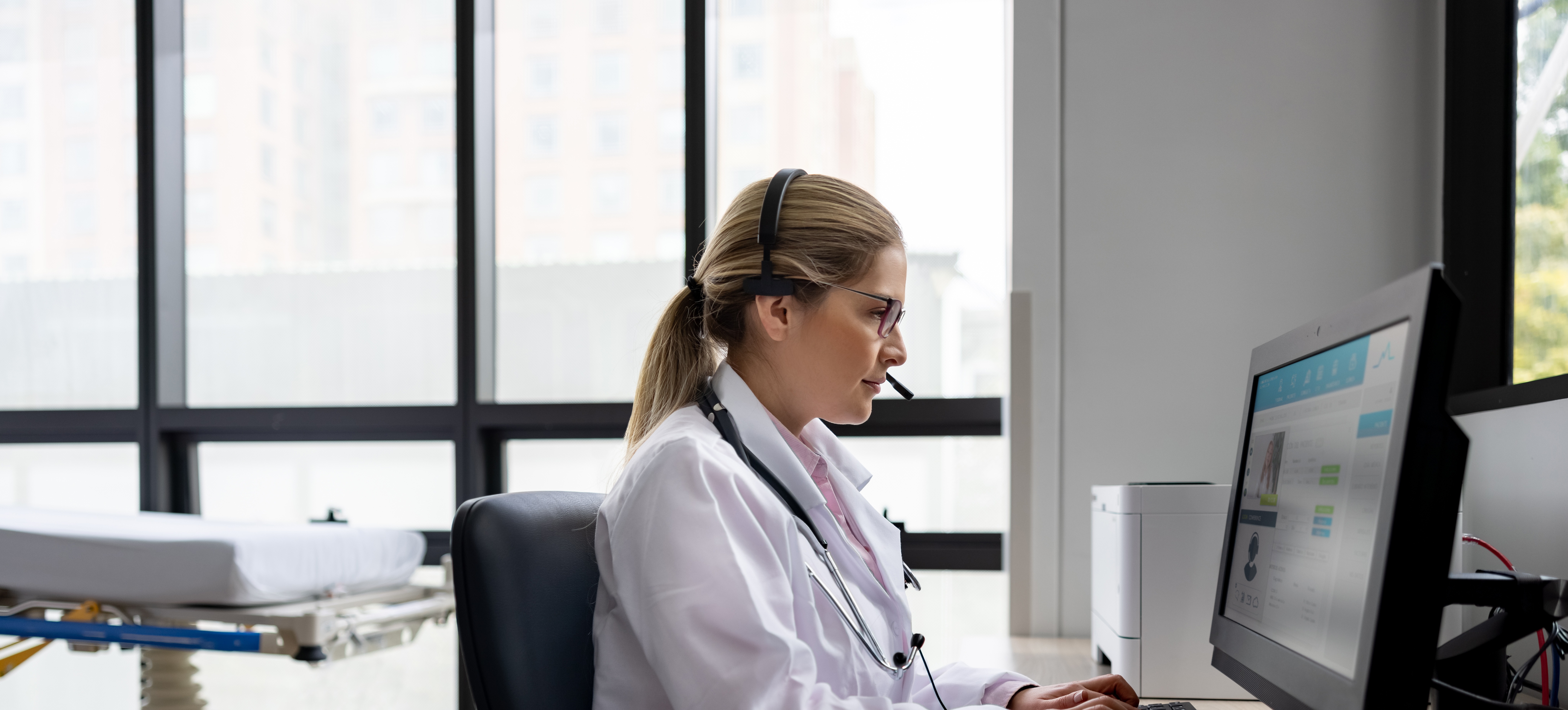[Featured Image]:  A telehealth nurse, wearing a white uniform, is sitting in front of their computer, communicating with a patient.