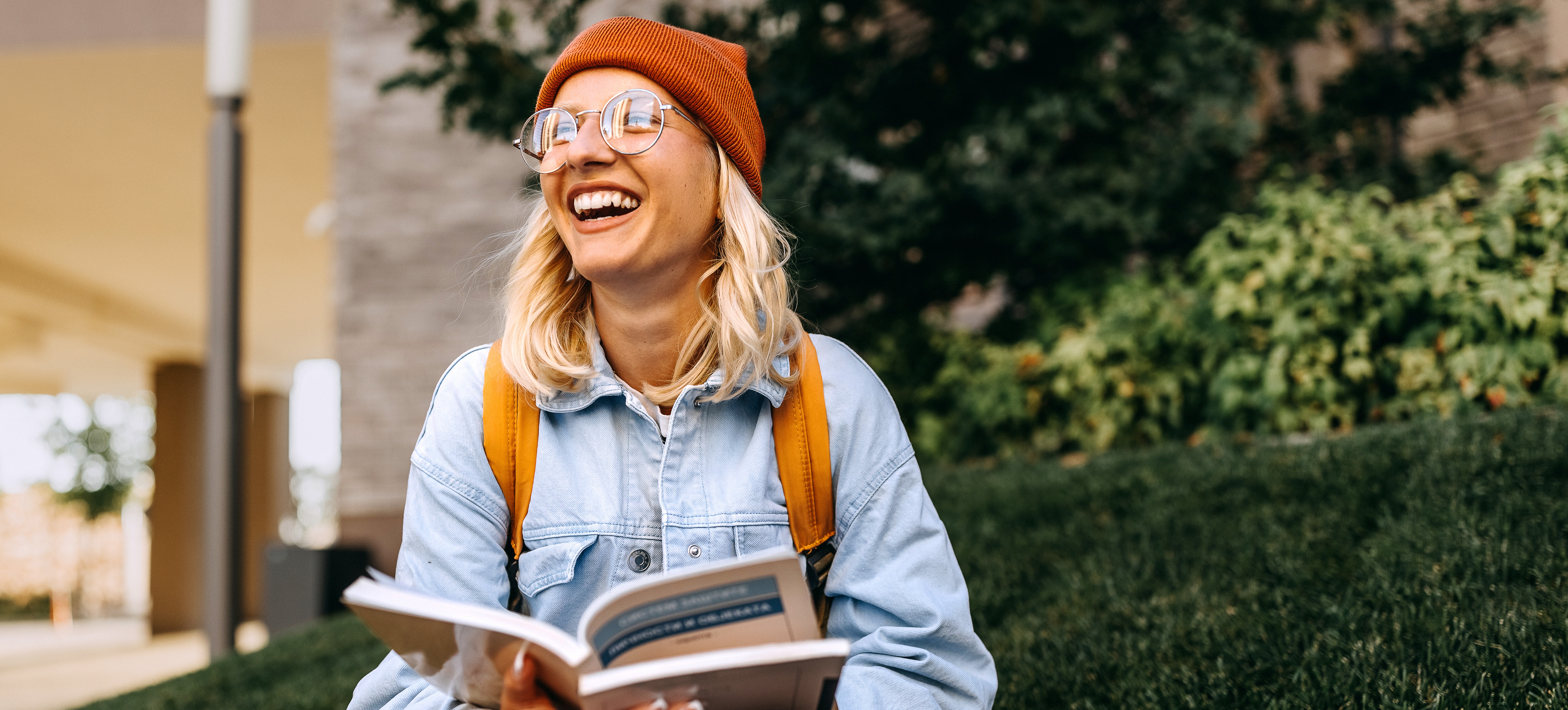 [Featured image] A humanities major, wearing glasses, studies outside with a textbook in their hands.