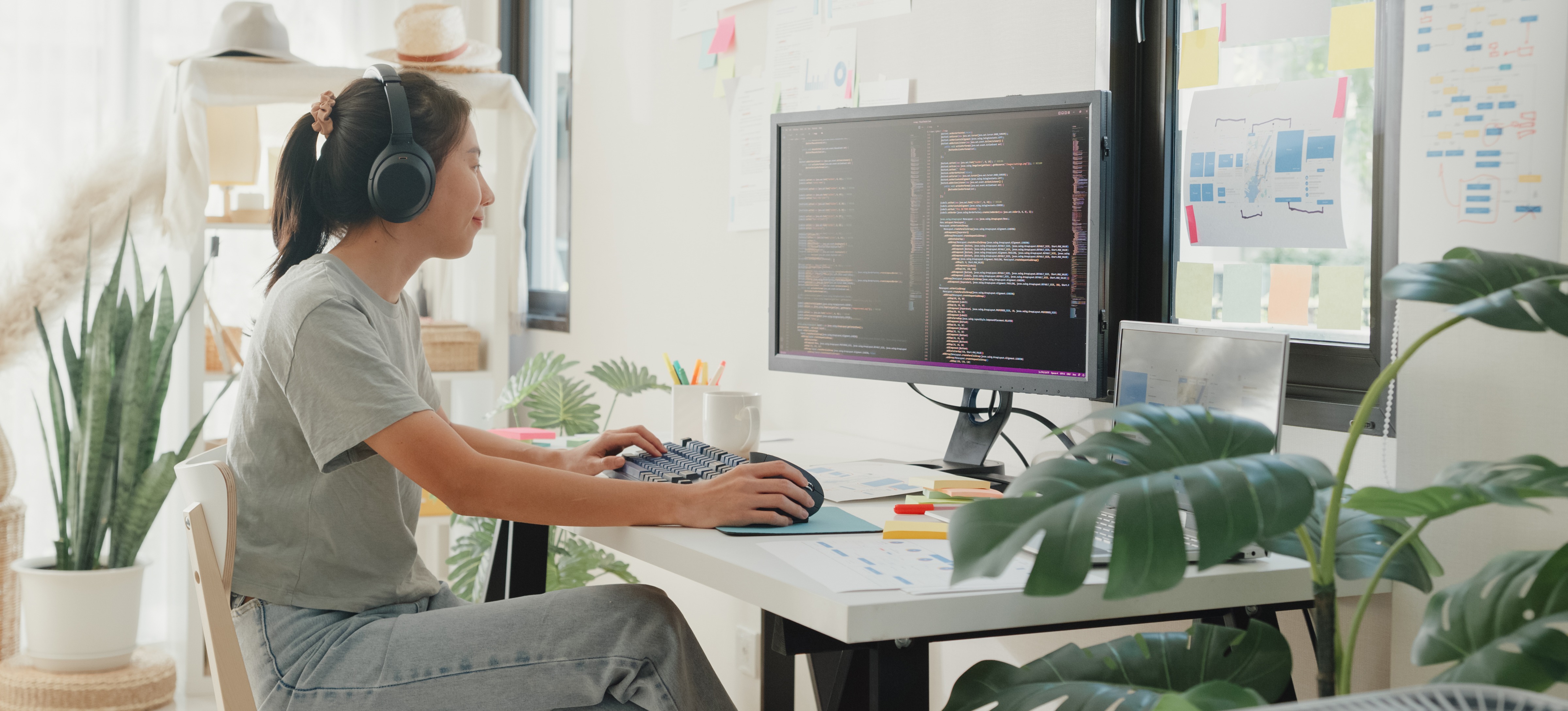 [Featured Image] After learning what is javascript used for, a young woman programmer sits at her desk in casual clothing, working on code on a computer in an office.
