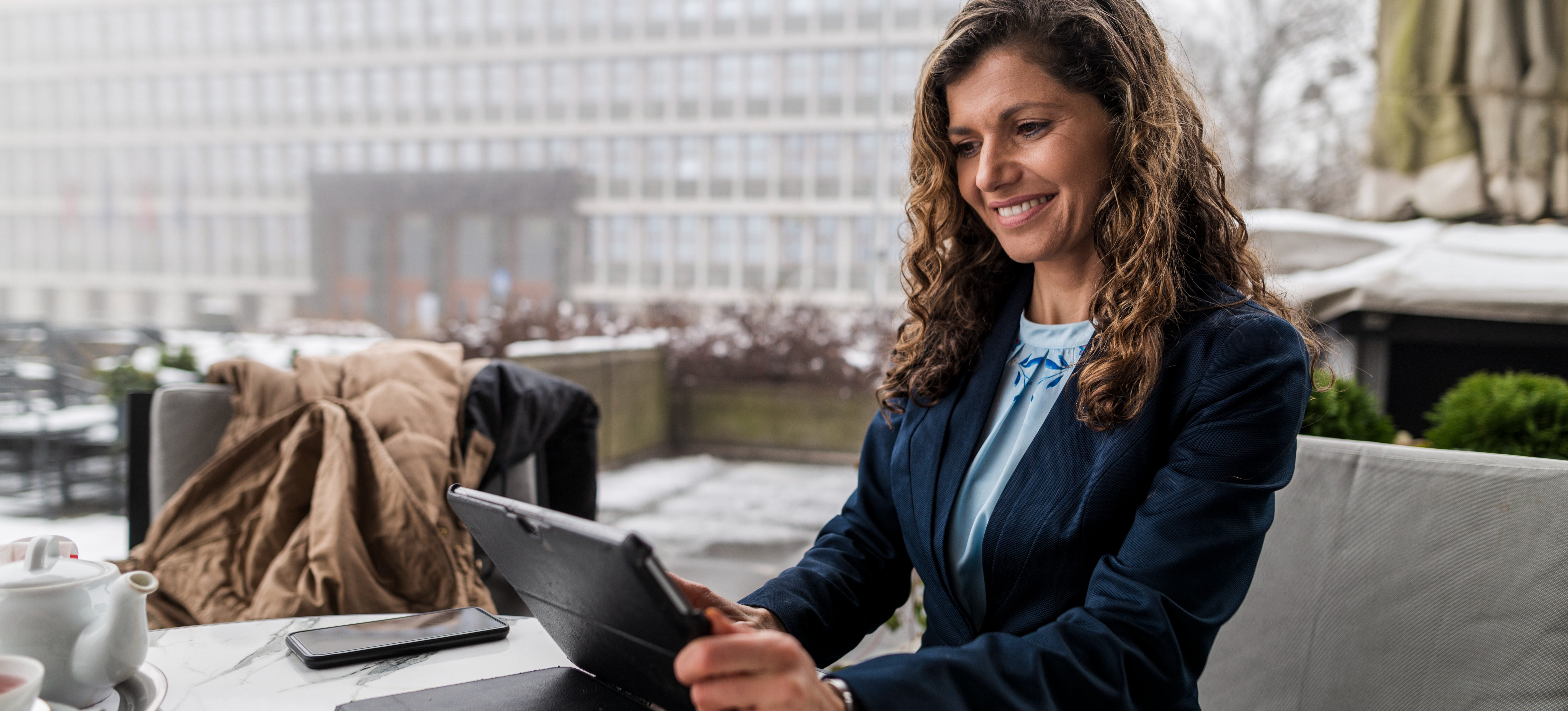 [Featured Image] A person sits at a cafe reading an article on their tablet in a European city.