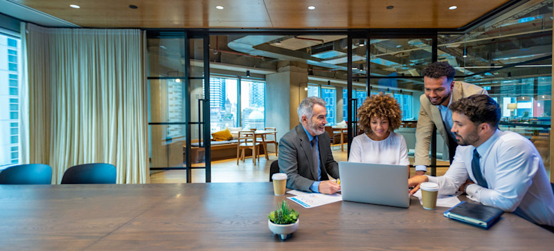 [Featured Image] A marketing manager discusses what marketing project is next with his team of three employees.  