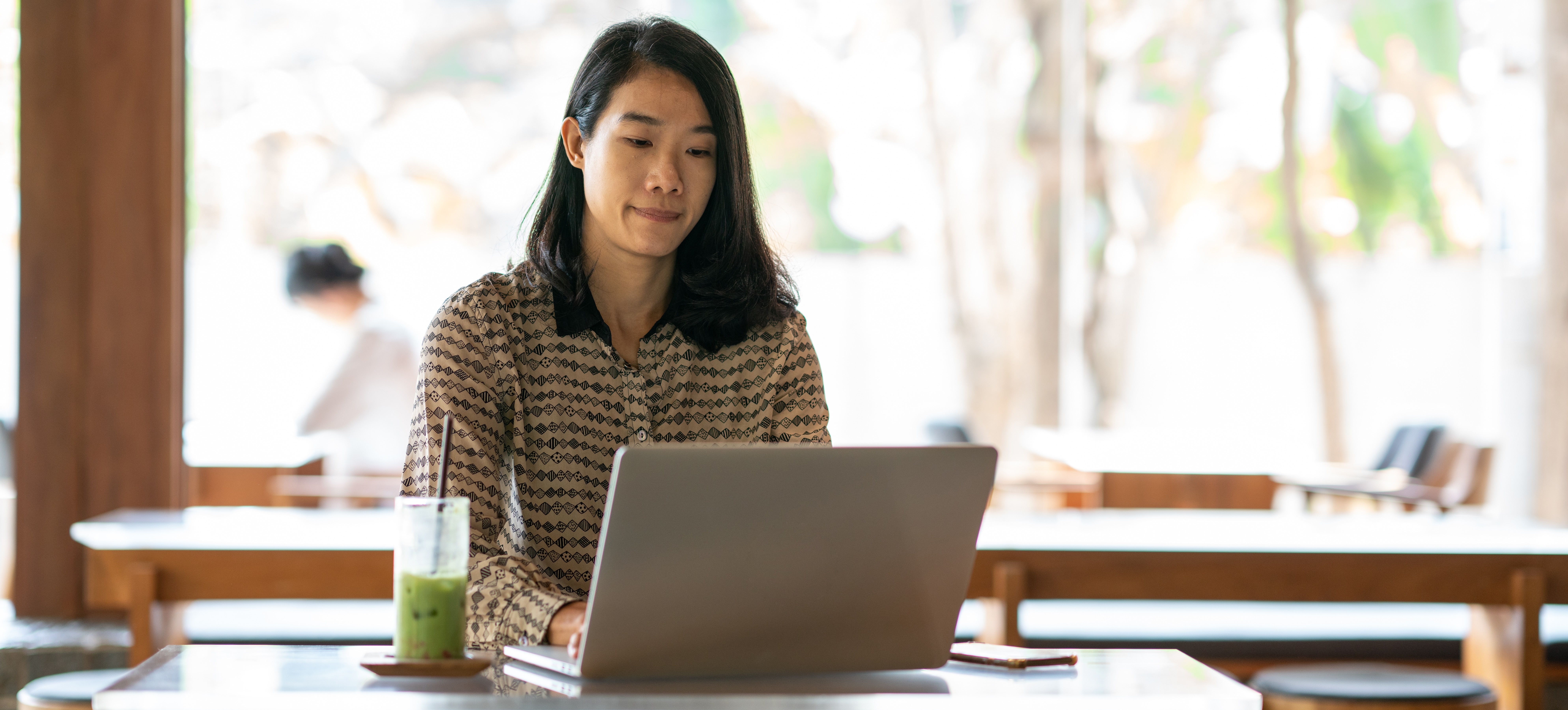 [Feature Image] A digital content creator works at a wood table in a coffee shop, providing digital content creation services on a freelance basis.
