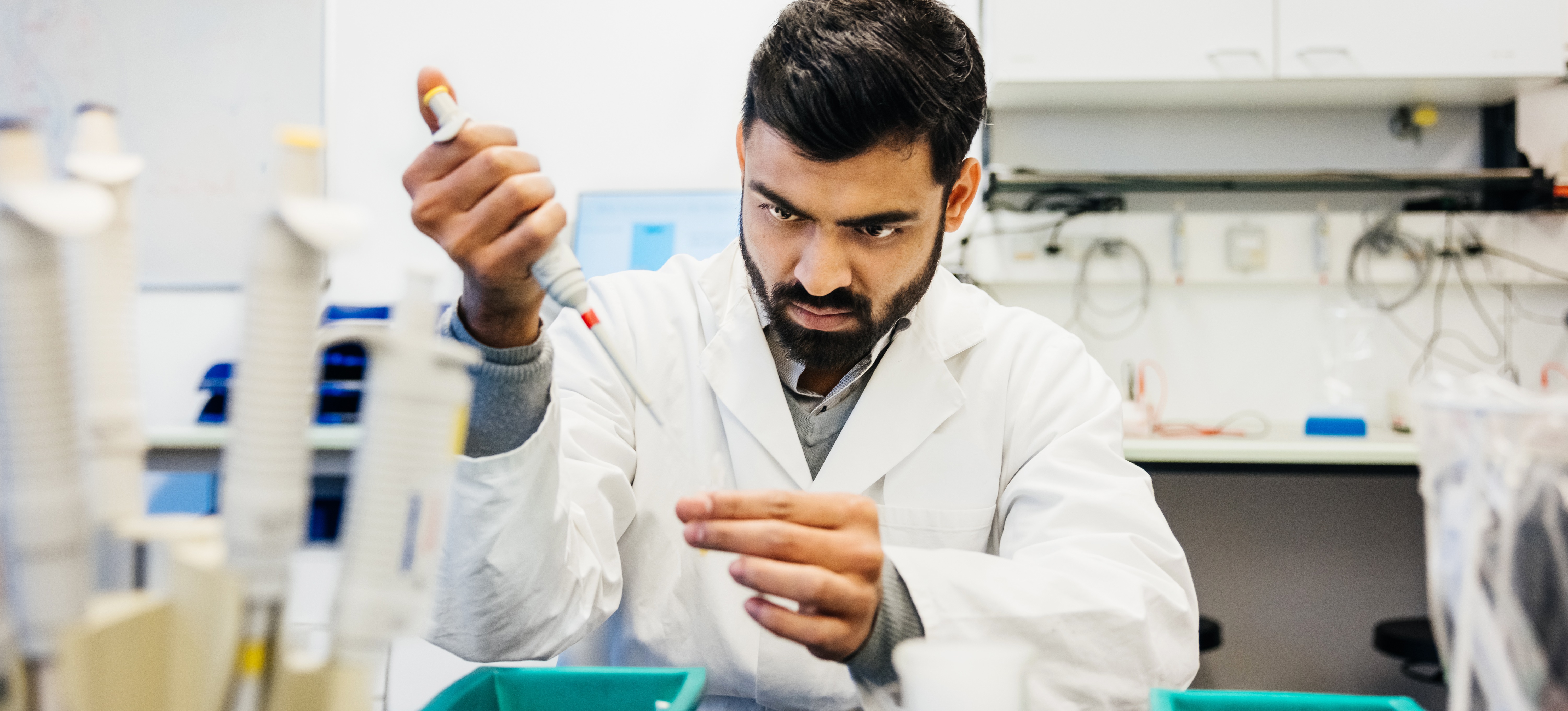 [Featured image] A man in a white lab coat uses a syringe to put liquid into a test tube.