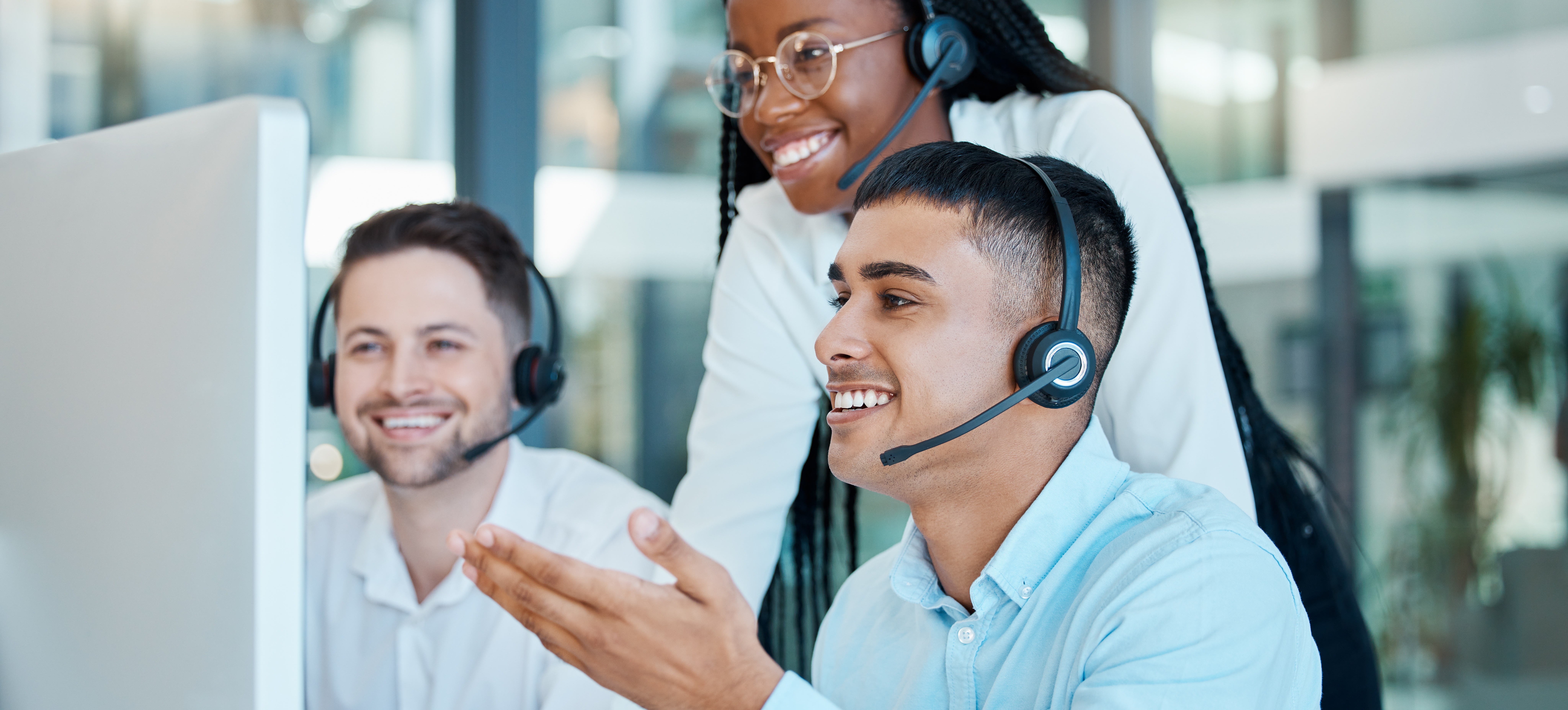 [Featured Image] Three smiling marketing professionals with headsets look at a computer monitor and manage customers using a CRM.
