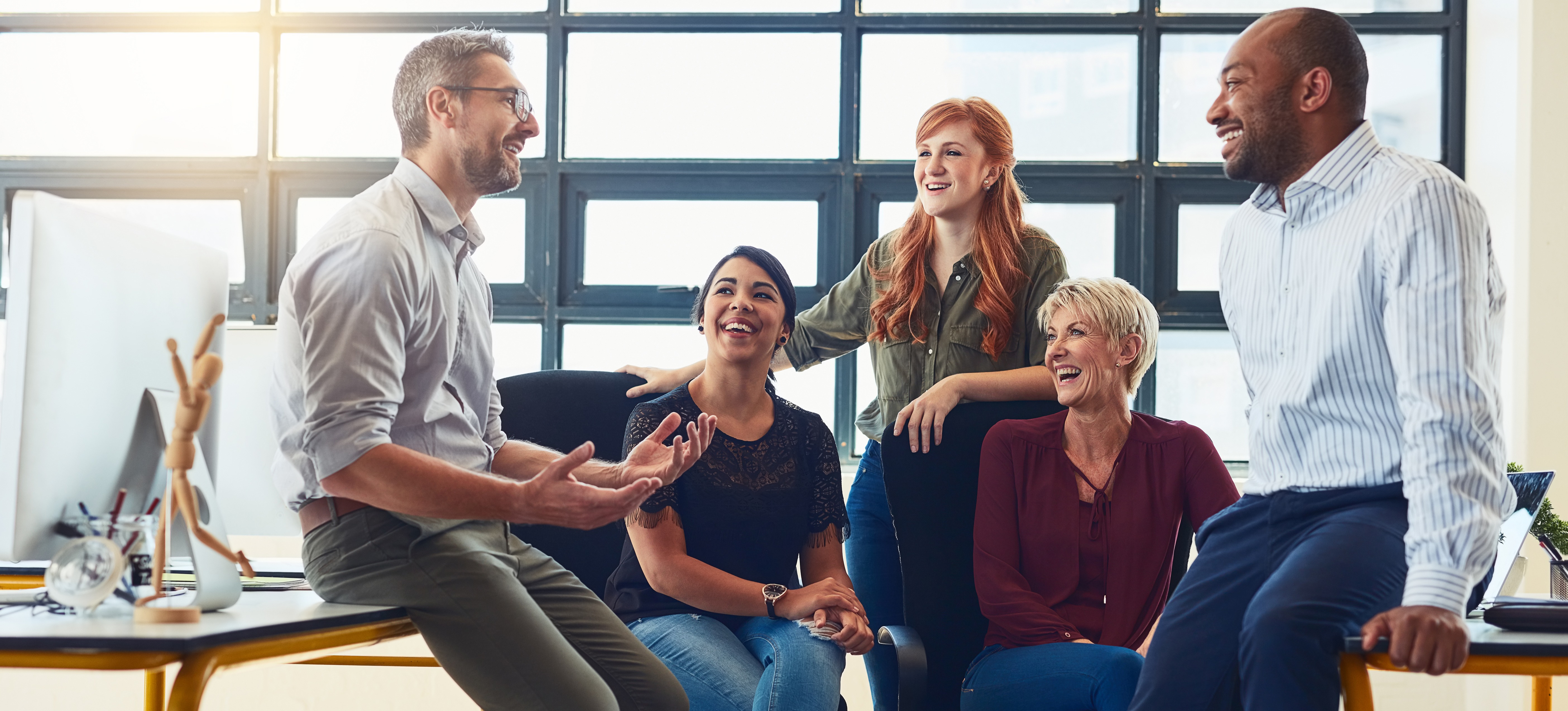 [Featured Image] A smiling team leader sits with colleagues in a workplace, demonstrating how to manage group discussions effectively.
