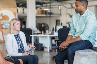 [Featured image] Three employees communicate during a casual meeting in their office.