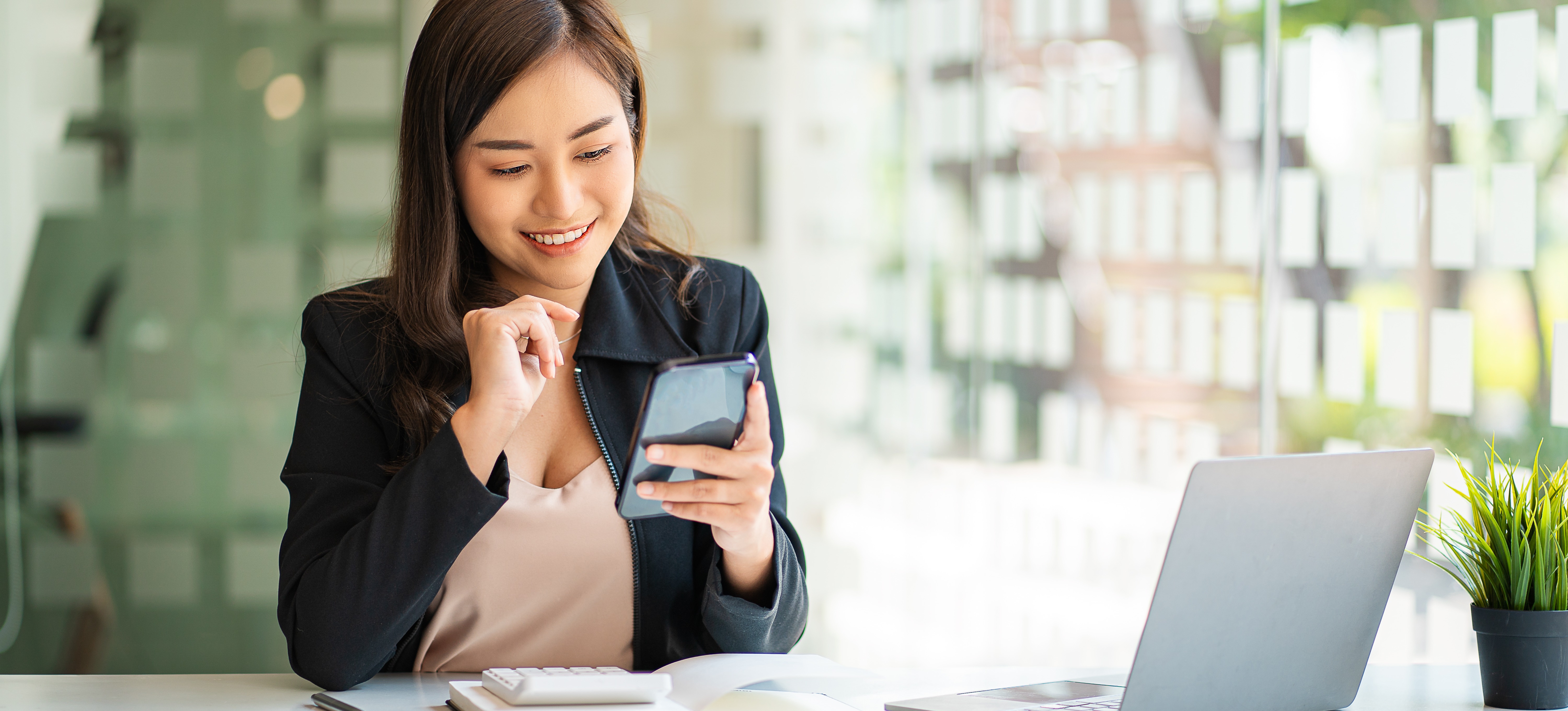 [Hauptbild] Eine lächelnde Softwareentwicklerin hält ein Android-Telefon mit VPN APK in der Hand, während sie an ihrem Schreibtisch in einem Büro sitzt
