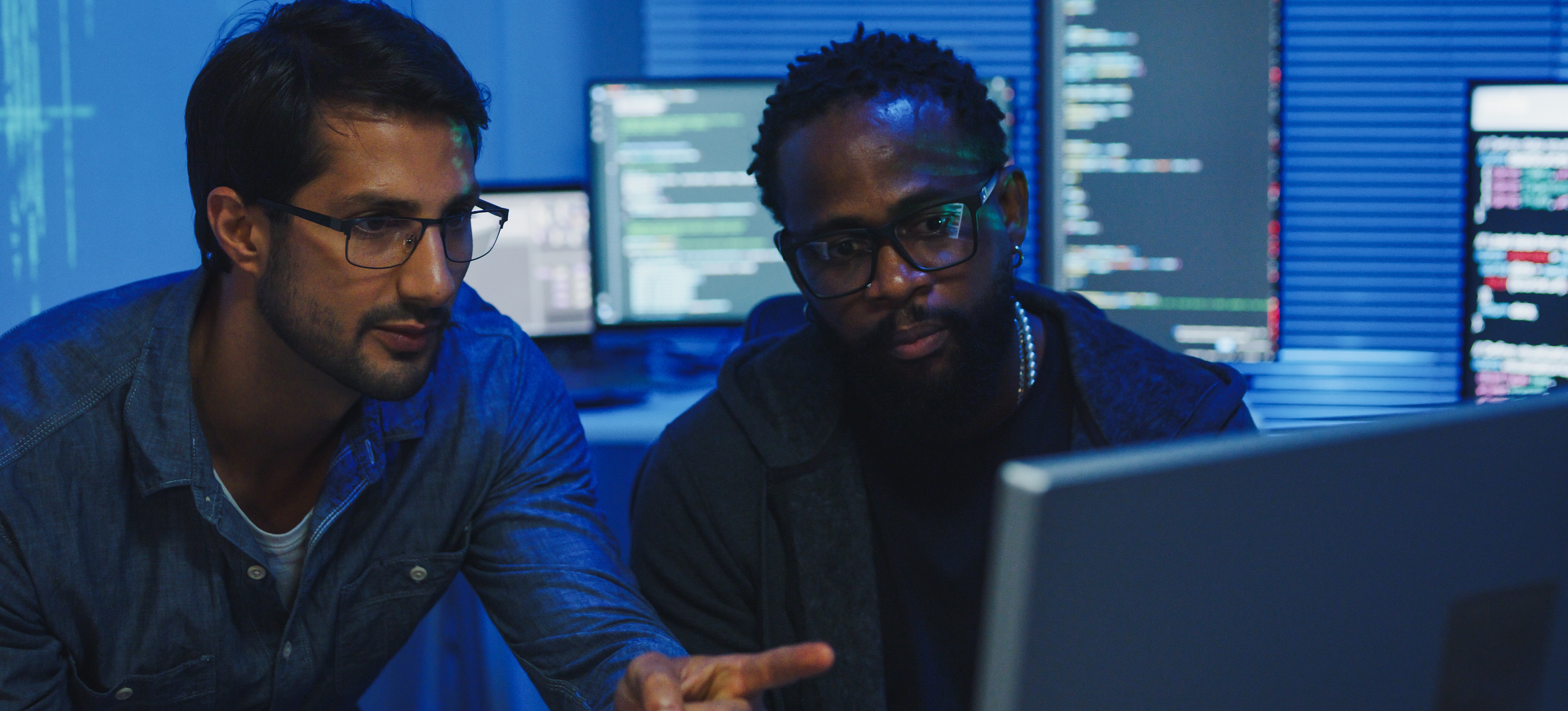 [Featured Image] Two smart contract developers work with Solidity as they look at a computer monitor and discuss the process.
