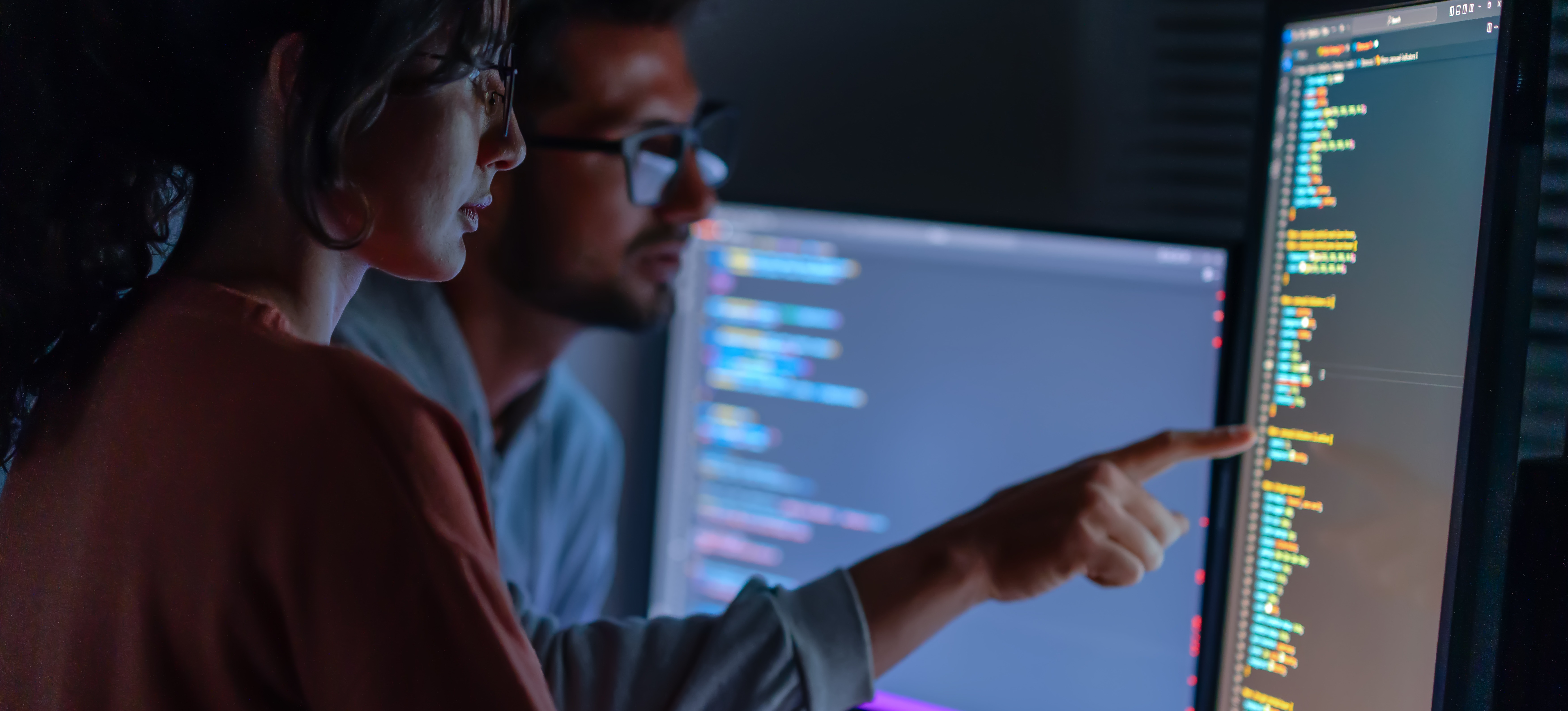 [Featured Image] Two types of software engineers look at a monitor as they review recently written code.
