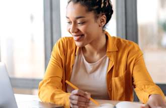A woman sits at a table with her laptop and researches how fast she can get a bachelor's degree online.
