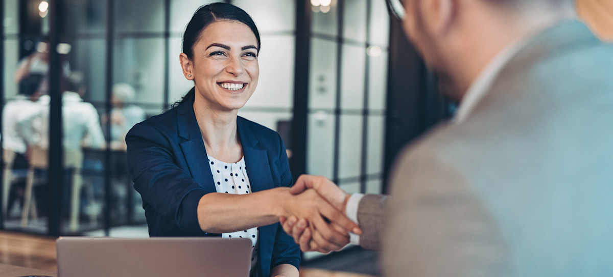 [Featured Image] An interviewer and a job applicant shake hands before delving into real estate interview questions. 