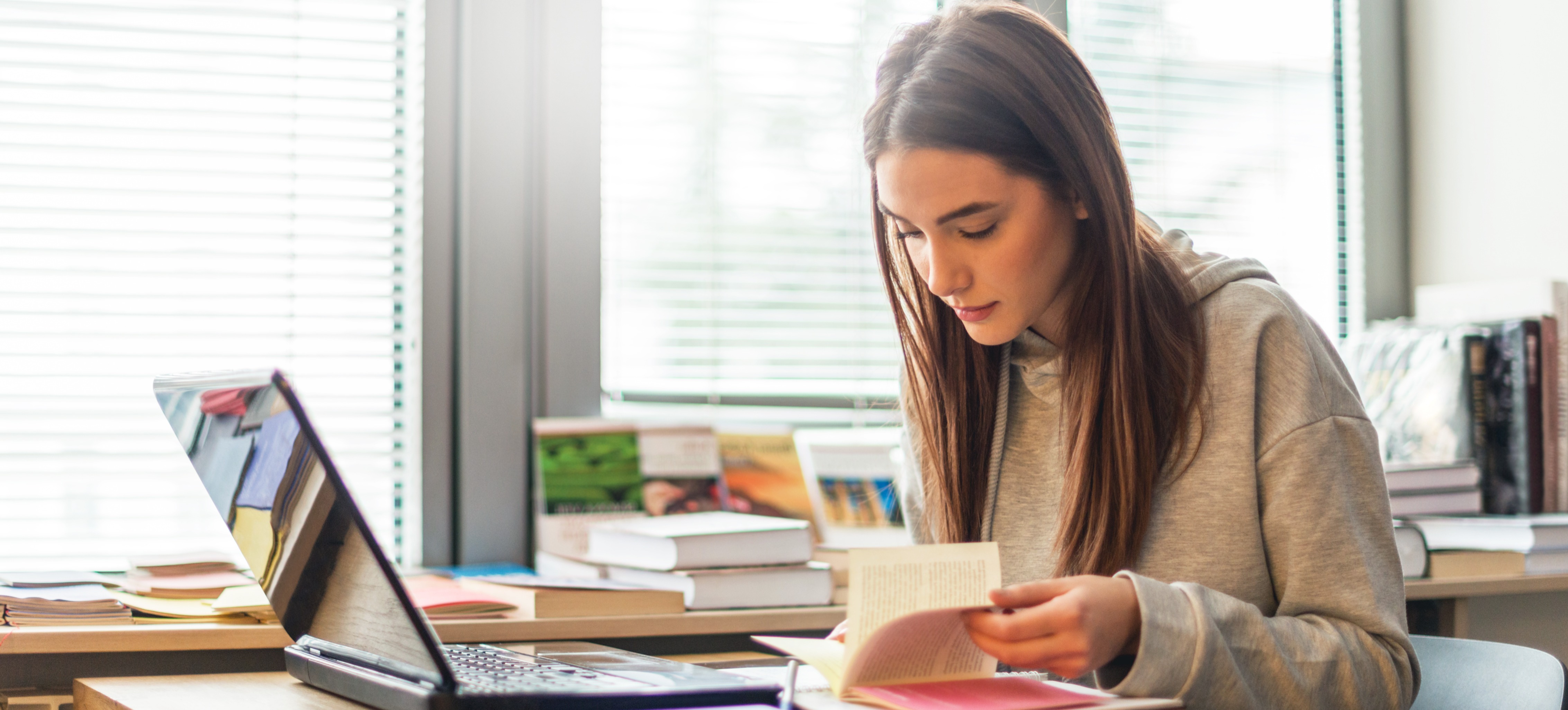 [Featured image] A learner wearing a beige sweatshirt studies for classes using a laptop and an open book.