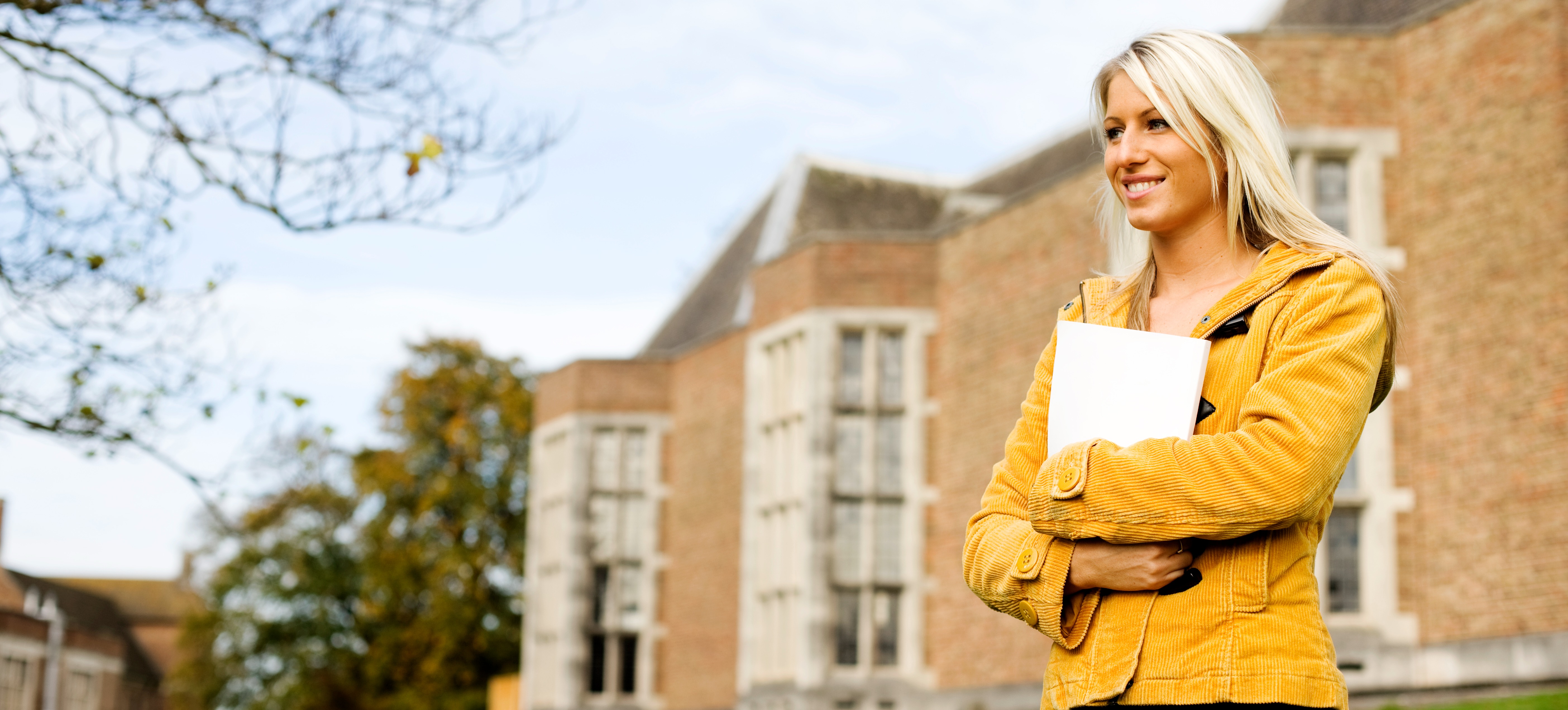 [Featured Image]: A student stands in front of a building on a university campus as they consider what rolling admission is.
