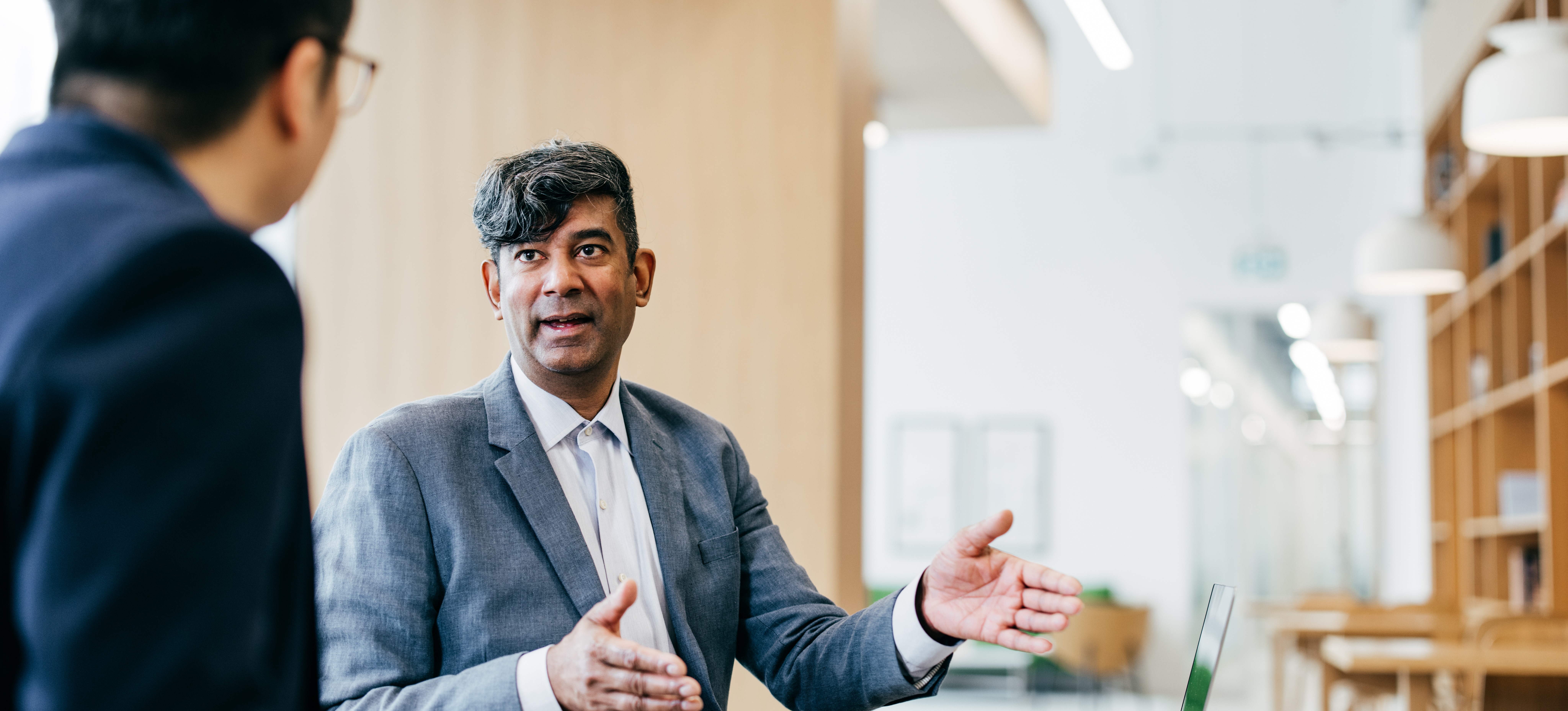 [Featured Image] Two professionals sit at a desk with a laptop for an interview discussing Infosys interview questions.