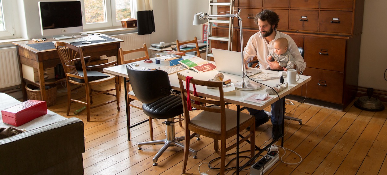 [Featured image] Employee working from home holding a baby as they types on their laptop