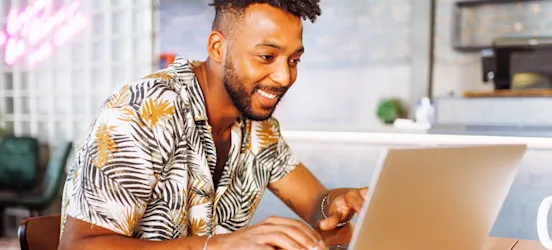[Featured Image] A marketer on their laptop in a cafe creates a new video action campaign for a client.