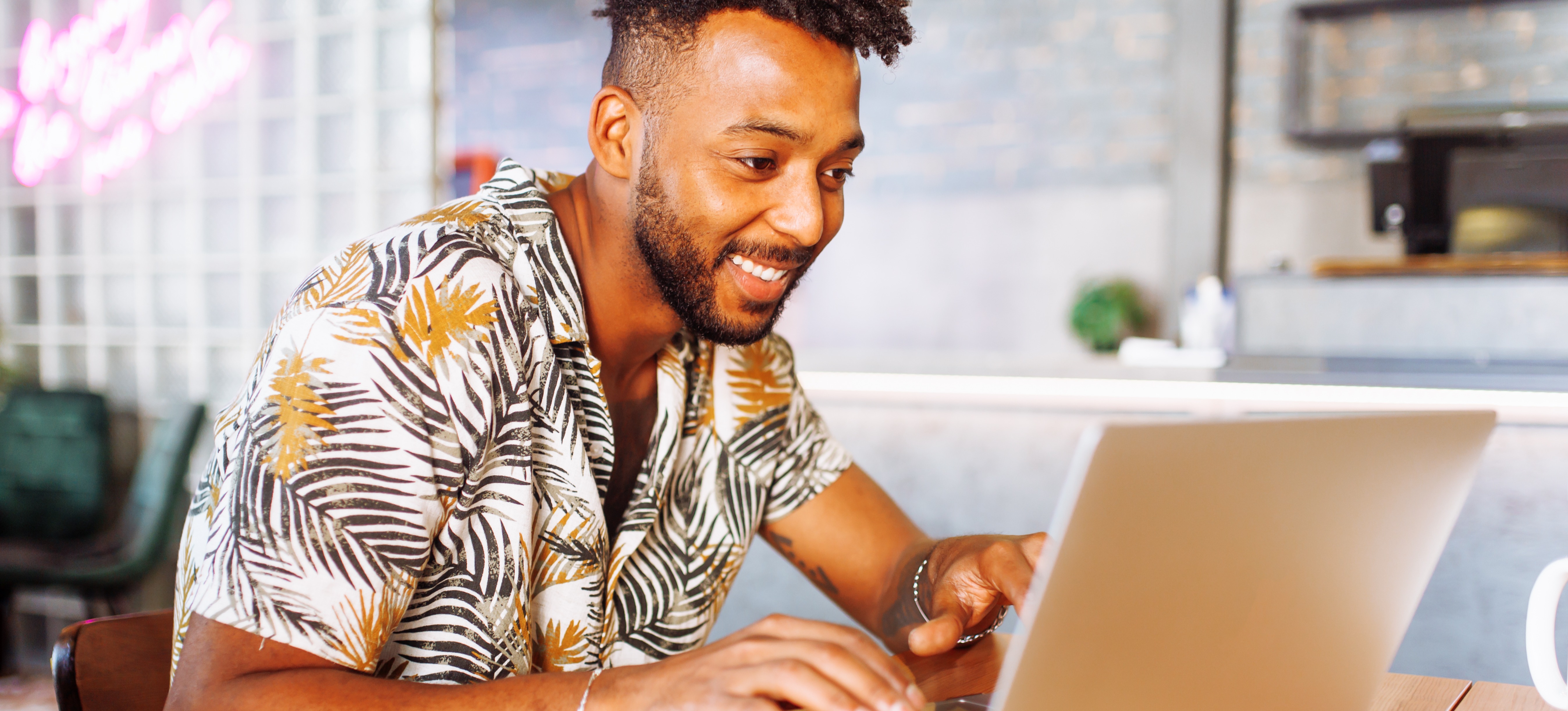[Featured Image] A marketer on their laptop in a cafe creates a new video action campaign for a client.