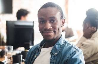 [Featured image] An employee wearing a white t-shirt under a blue denim button-down smiles during an employee development training class.