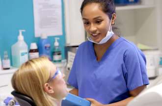 [Featured Image] A dental assistant speaks with a patient in the dentist's office.